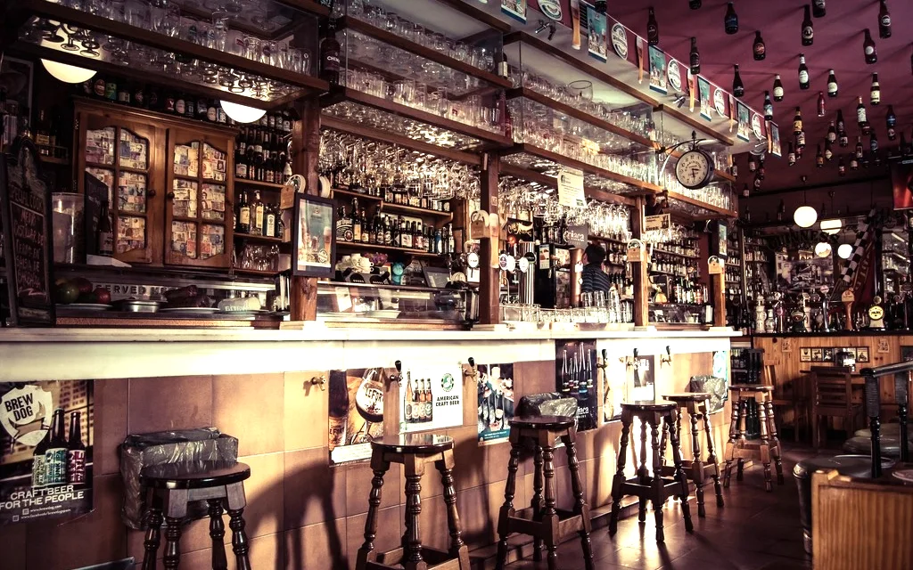 Balcão de bar com banquetas e prateleira de bebidas ao fundo