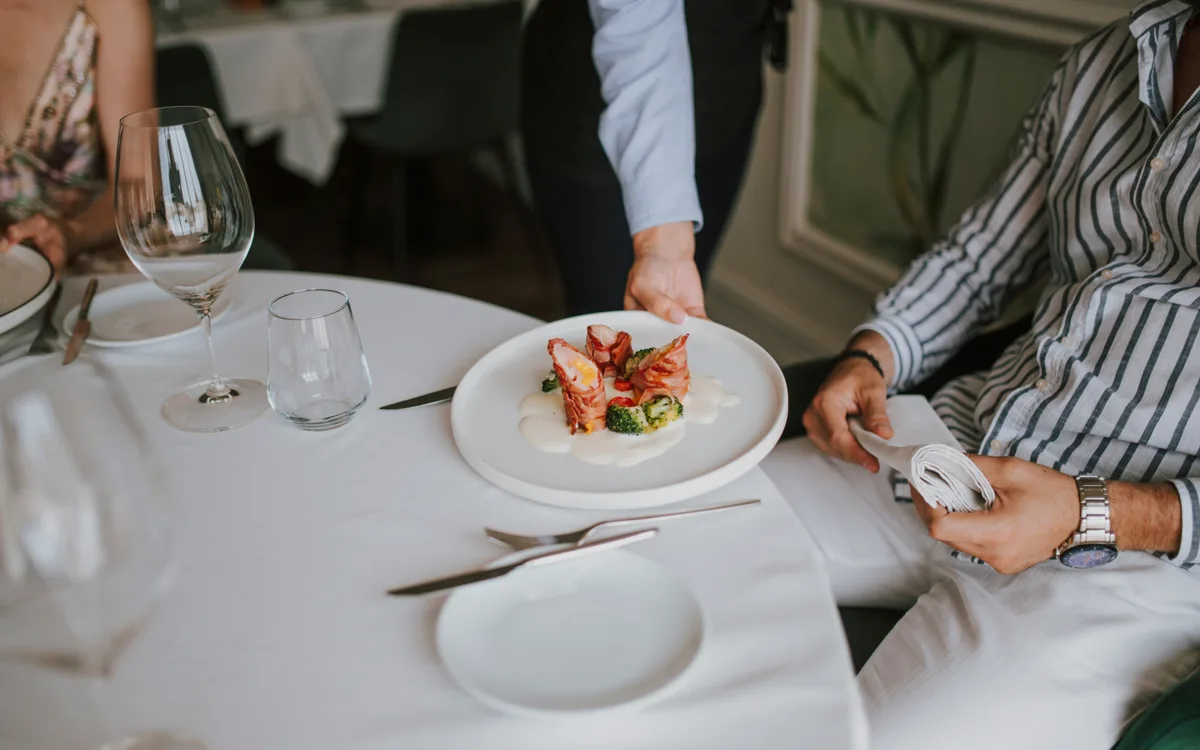 Garçom servindo um prato a um cliente na mesa de um restaurante
